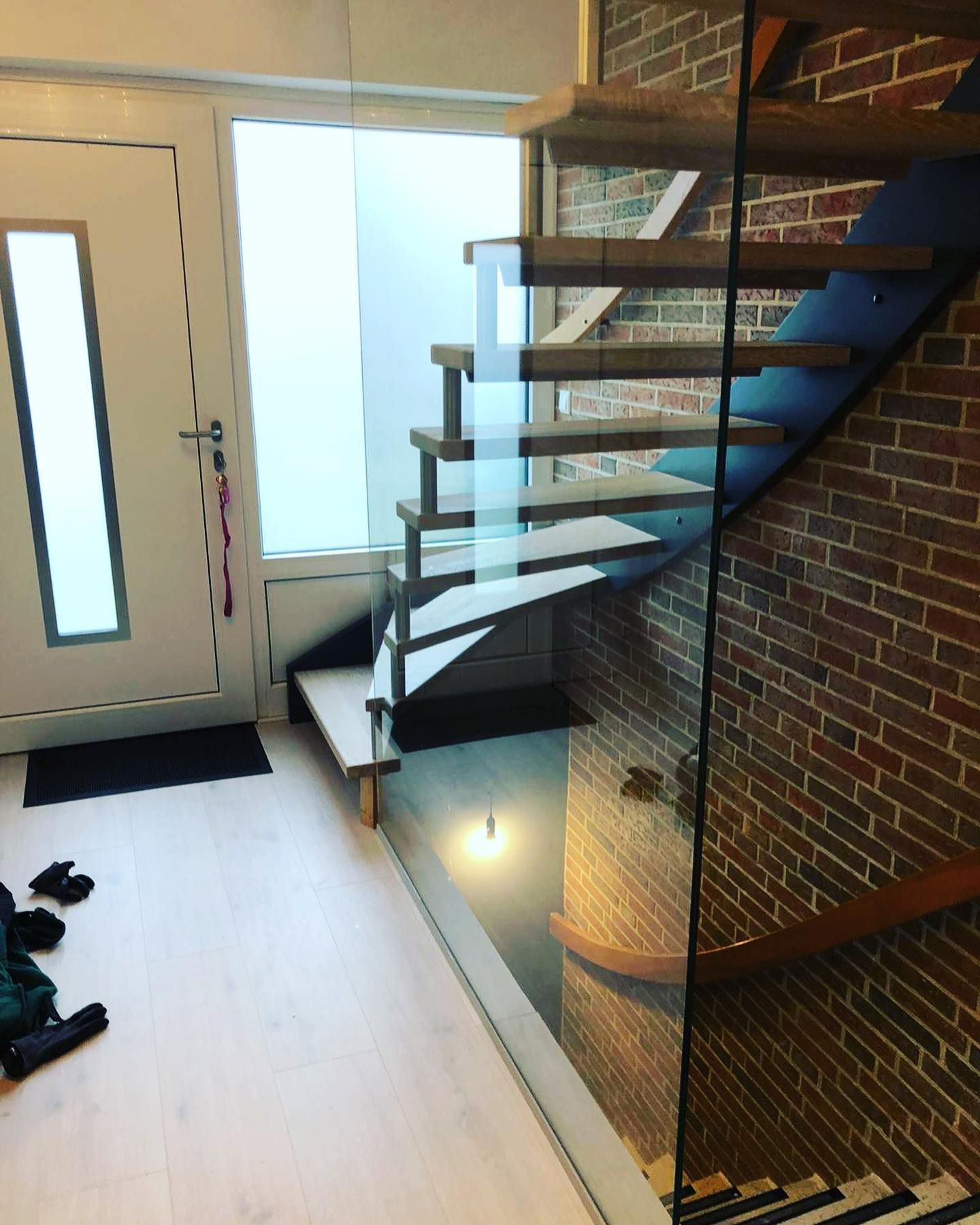 Eine Treppe mit einem Glasgeländer in einem Flur neben einer Backsteinwand.