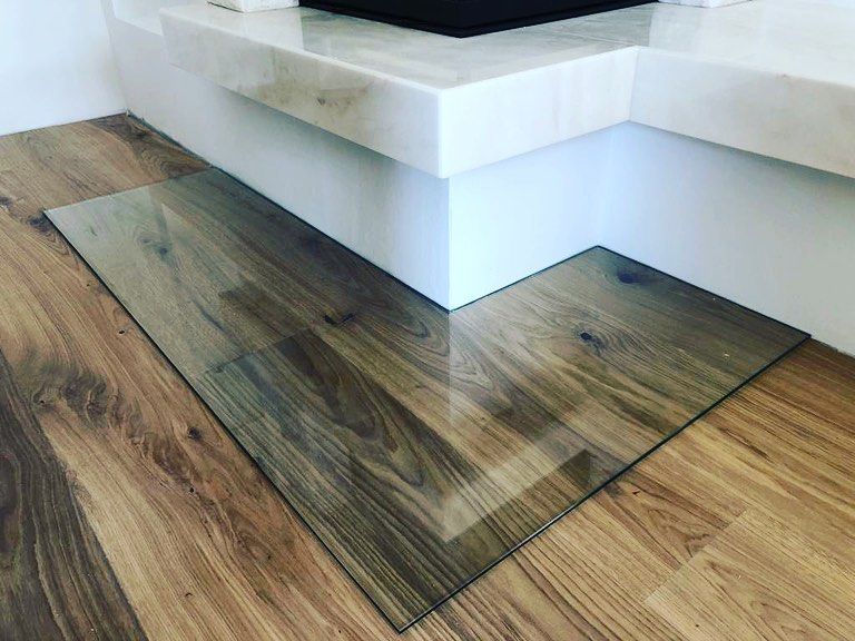 Eine Glasmatte liegt auf einem Holzboden neben einem Kamin.