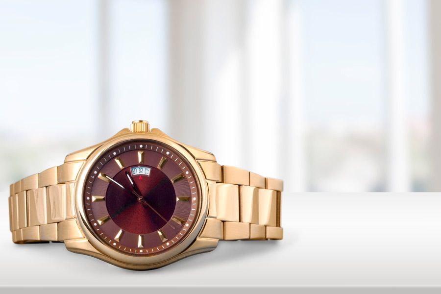 Un reloj de oro con esfera roja está sobre una mesa blanca.