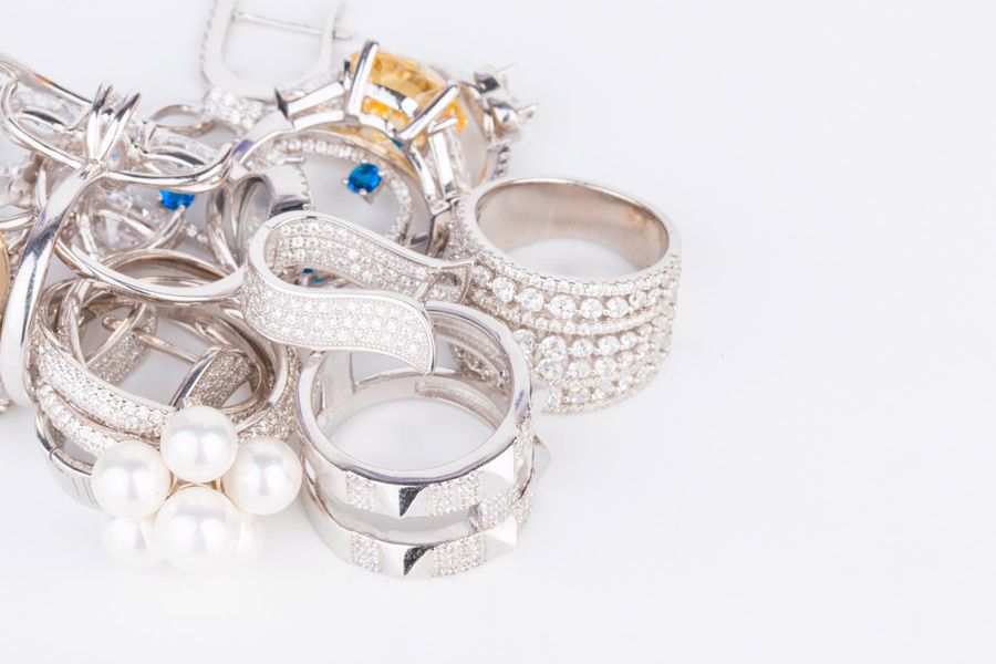 Una pila de anillos de plata y perlas sobre una superficie blanca.