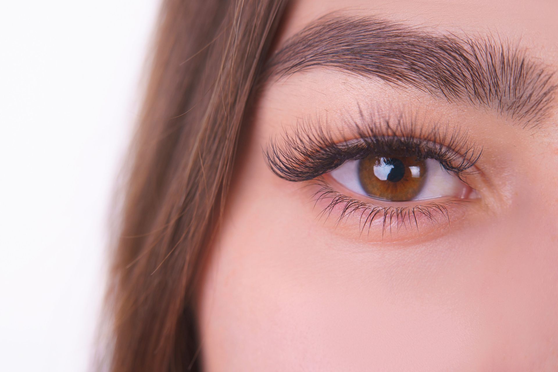 Primer plano del ojo de una mujer con iris marrón, pestañas y cejas oscuras sobre un fondo blanco.