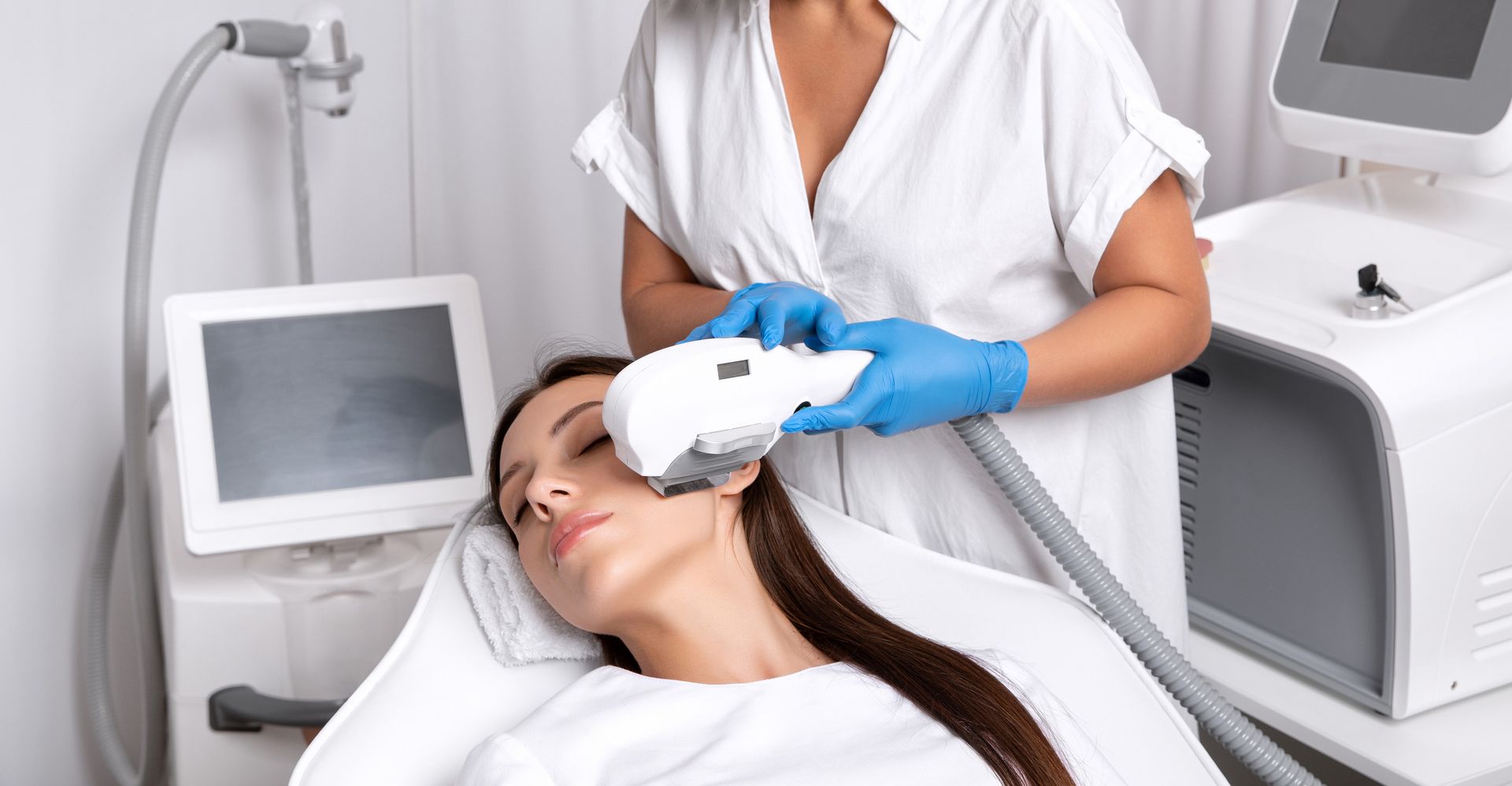 Una mujer recibe un tratamiento facial con un dispositivo portátil de una persona que usa guantes en un entorno médico.