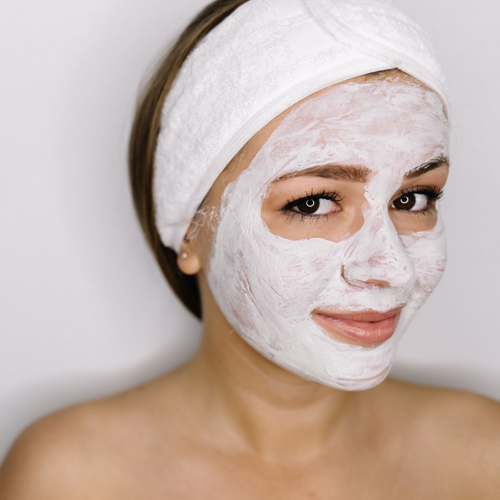 Mujer con mascarilla blanca y diadema, sonriendo. Tiene el pelo y la piel castaños, sobre un fondo blanco.