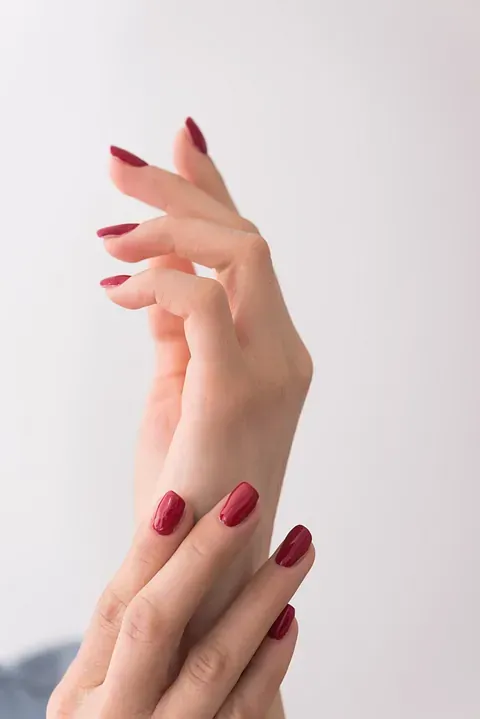 Manos con esmalte de uñas rojo, posando graciosamente sobre un fondo blanco.