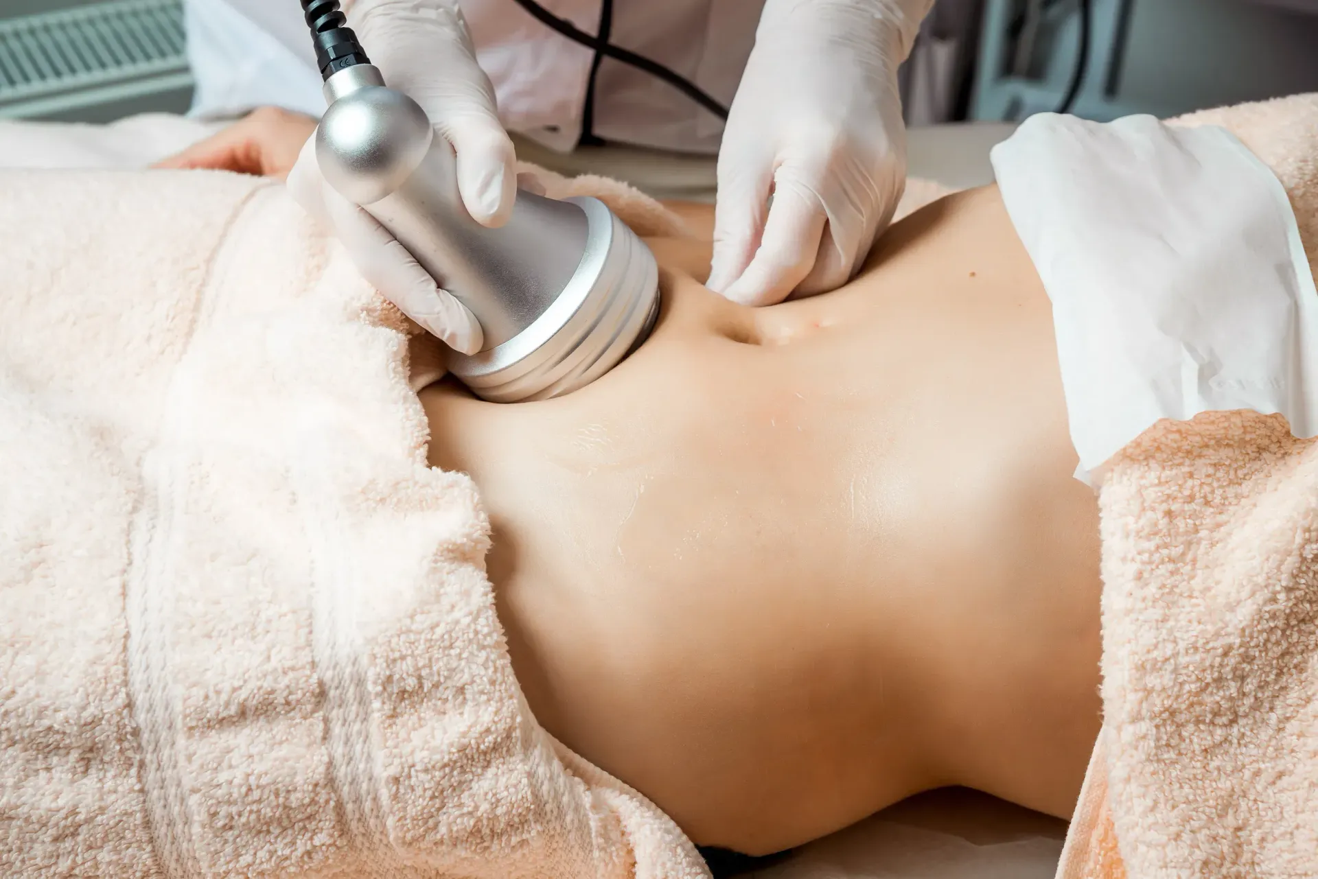Persona recibiendo un tratamiento de modelado corporal en el abdomen. El técnico utiliza un dispositivo portátil con guantes.