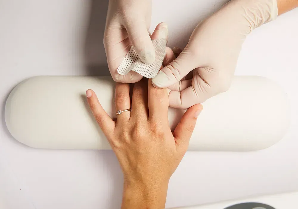Manos con guantes aplicando un vendaje a un dedo sobre una superficie blanca.