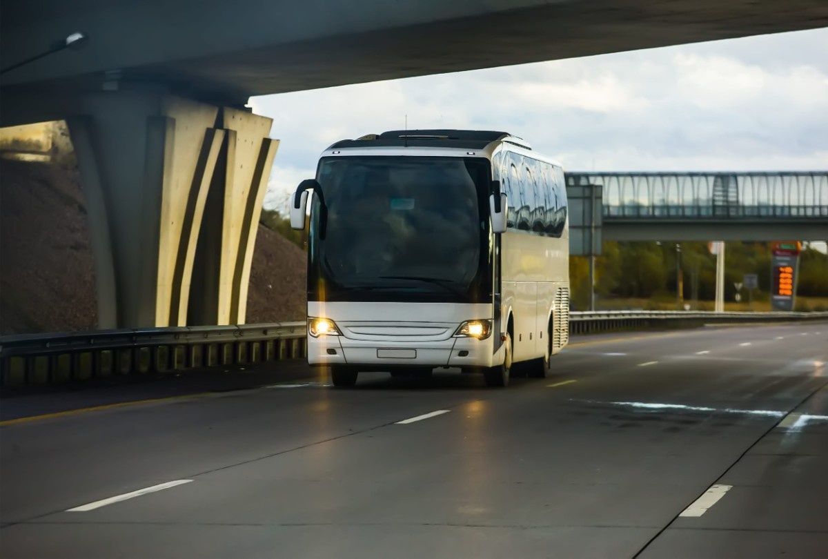 Un autobús blanco circula por una autopista de varios carriles bajo un gran puente de hormigón.