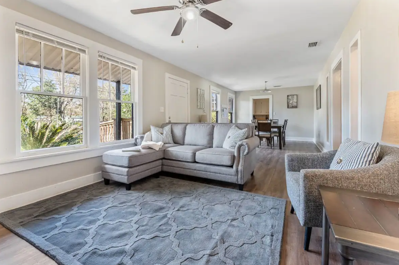 A living room with a sectional couch , chairs , a rug and a ceiling fan.