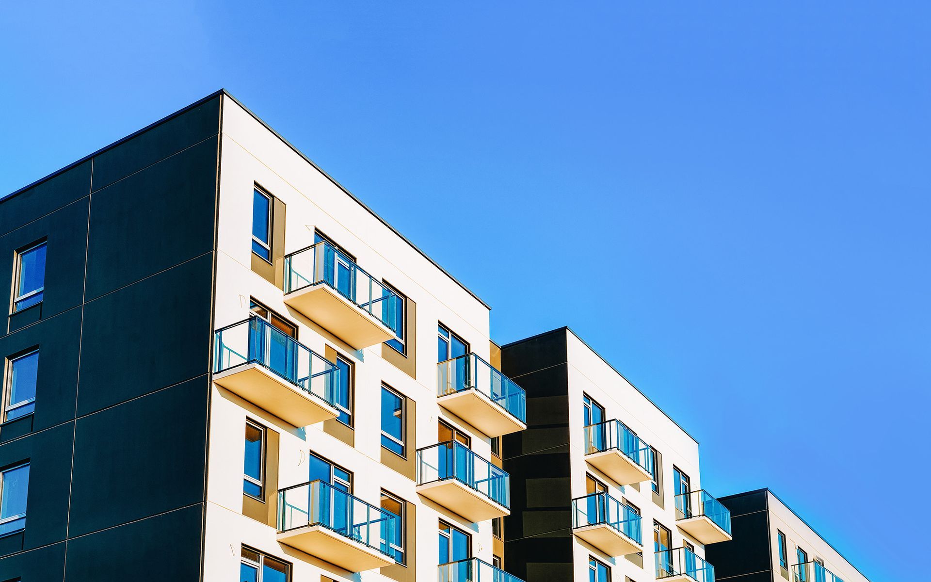 Ein großes Wohnhaus mit Balkonen vor einem blauen Himmel.