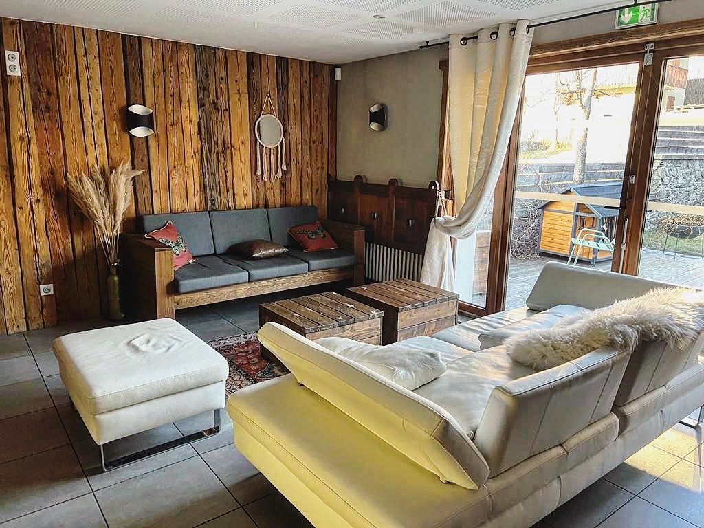 Salon confortable avec mur en bois, deux canapés et poufs. Une grande fenêtre offre une vue agréable.