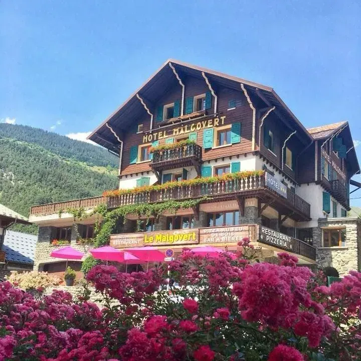 Hôtel en montagne, orné de fleurs et d'auvents roses sous un ciel bleu.