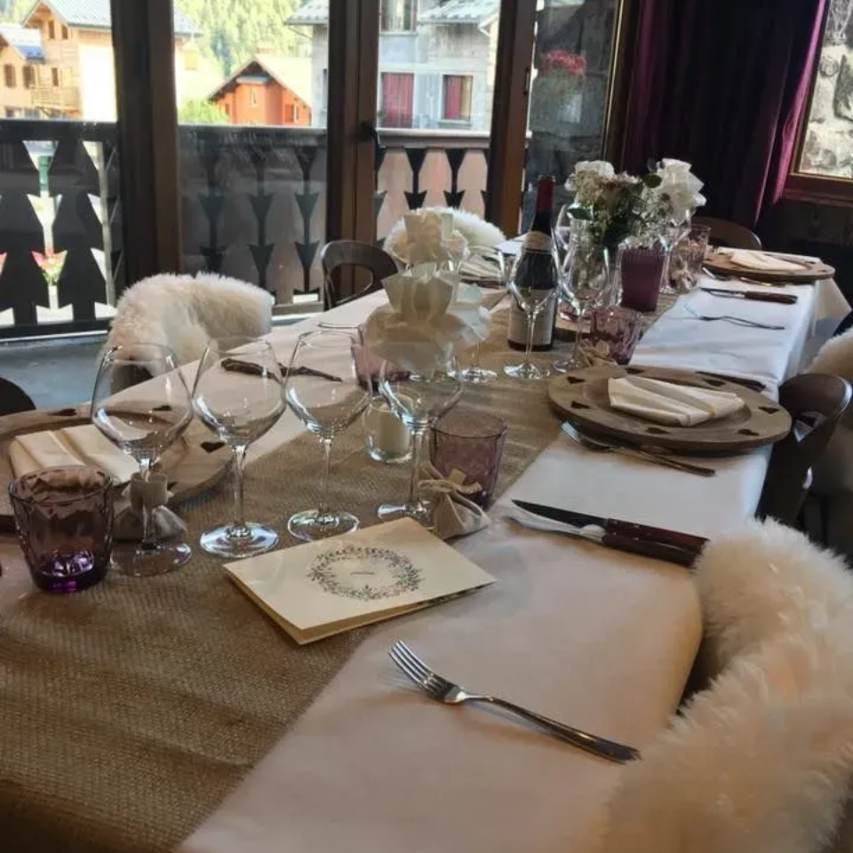 Table à manger dressée pour un repas formel. Nappes en toile de jute et lin blanc, verres à vin, fleurs et couverts.