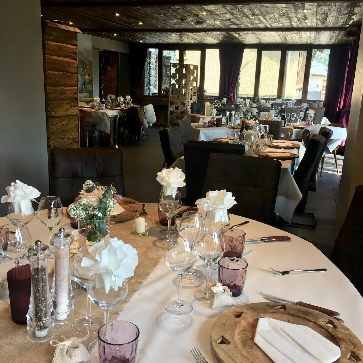 Salle à manger d'un restaurant avec tables dressées pour un repas. Les tables sont décorées de fleurs, de verres et de vaisselle.