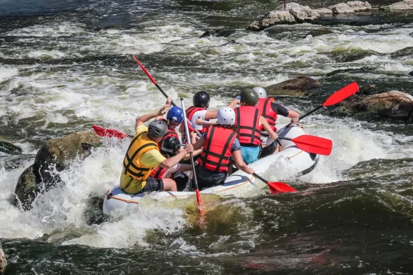 Rafting en eaux vives : un groupe de personnes à bord d'un radeau navigue sur des rapides en pagayant avec des pagaies rouges.