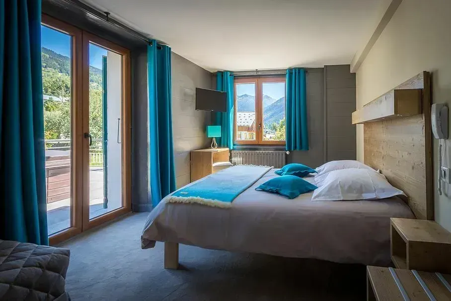 Chambre d'hôtel avec lit, touches de turquoise, balcon et vue sur la montagne.