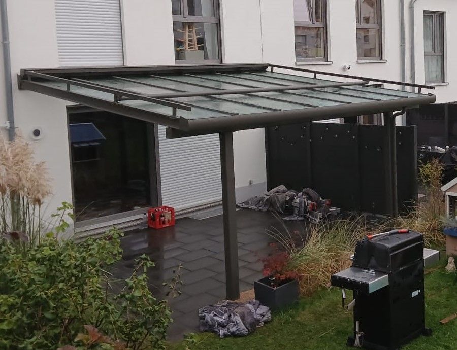 Terrassen-Überdachung: Ein Grill steht unter einem Vordach im Hinterhof eines Hauses.