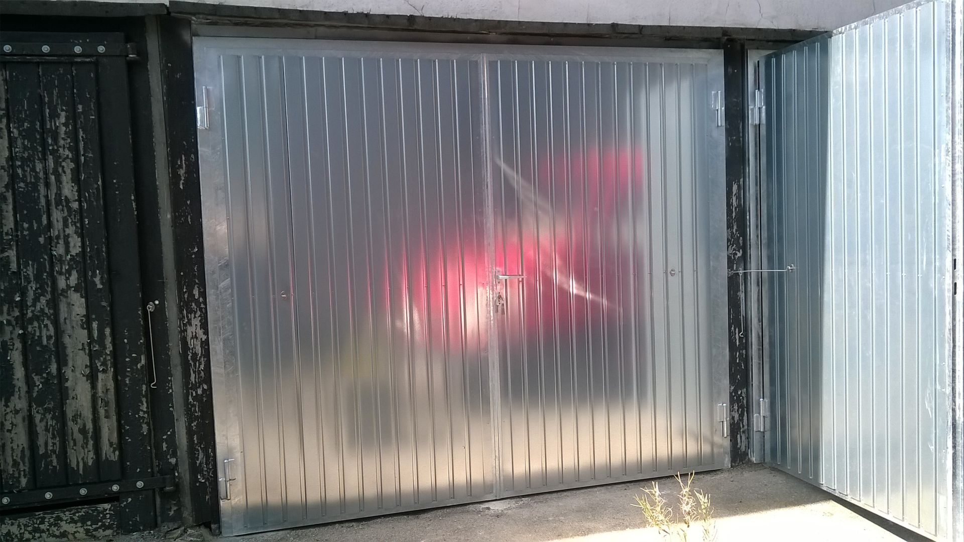 Ein rotes Auto steht in einer Garage mit durchsichtigem Tor.