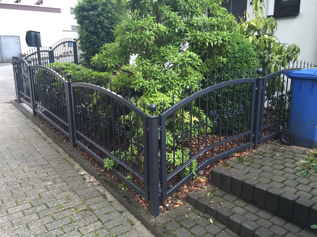 Ein blauer Mülleimer steht neben einem schwarzen Zaun