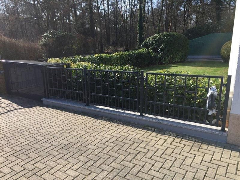 Eine gemauerte Auffahrt mit einem Zaun und Büschen im Hintergrund