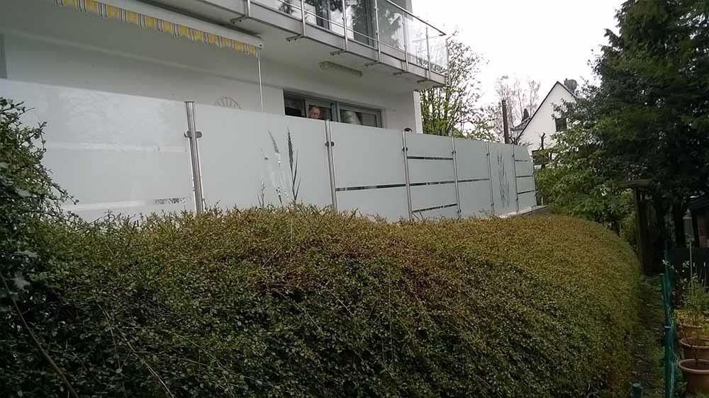 Hinter einer Hecke befindet sich ein weißes Gebäude mit Balkon.