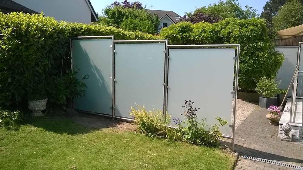 Ein weißer Zaun mit Edelstahlrahmen steht inmitten eines üppig grünen Hofes.