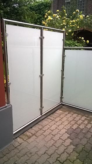 Auf einem Gehweg aus Backsteinen steht ein weißer Zaun mit einem Rahmen aus Edelstahl.