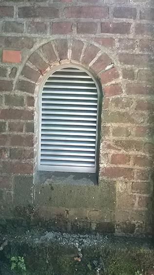 Ein kleines Fenster in einer Backsteinmauer mit einem Metallladen.