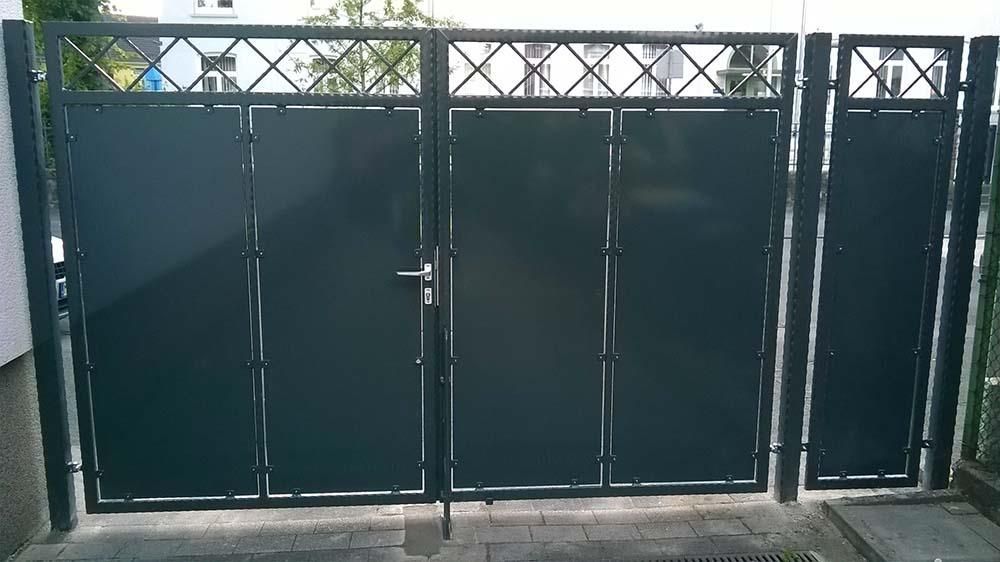 Auf einer gepflasterten Auffahrt steht ein schwarzes Metalltor.