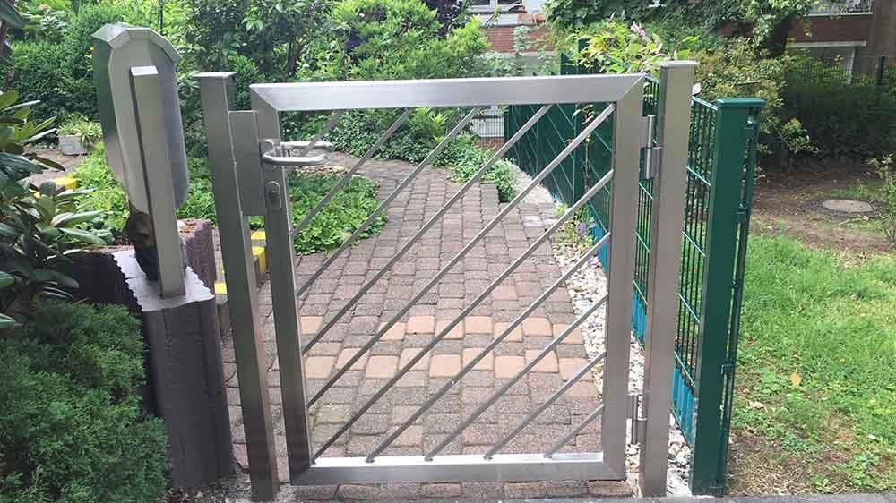 Durch ein Edelstahltor gelangt man auf einen gemauerten Gehweg.