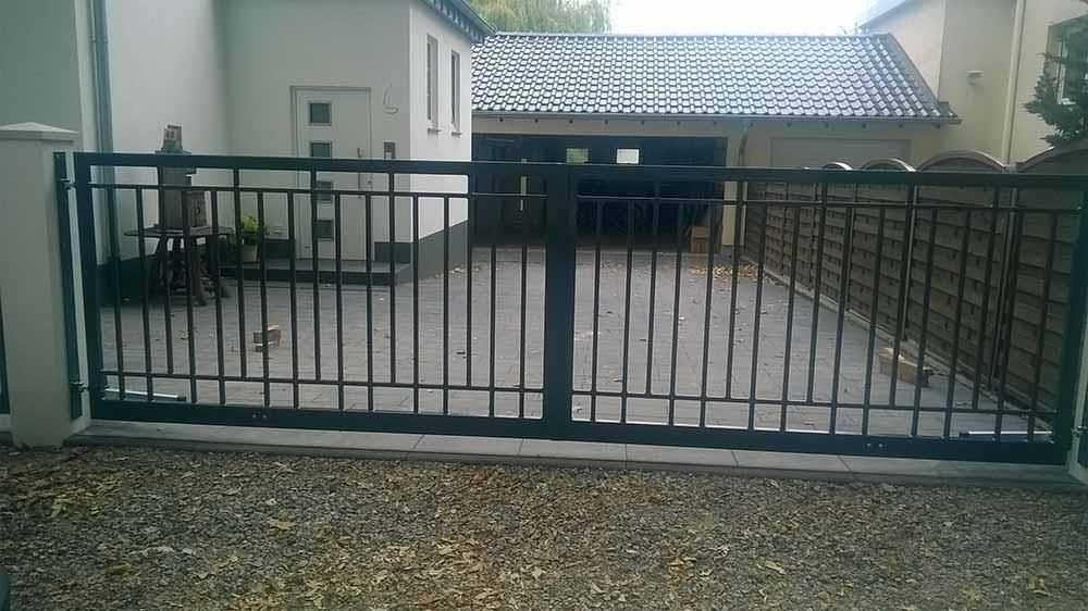 Ein schwarzer Zaun umgibt eine Kiesauffahrt vor einem Haus.