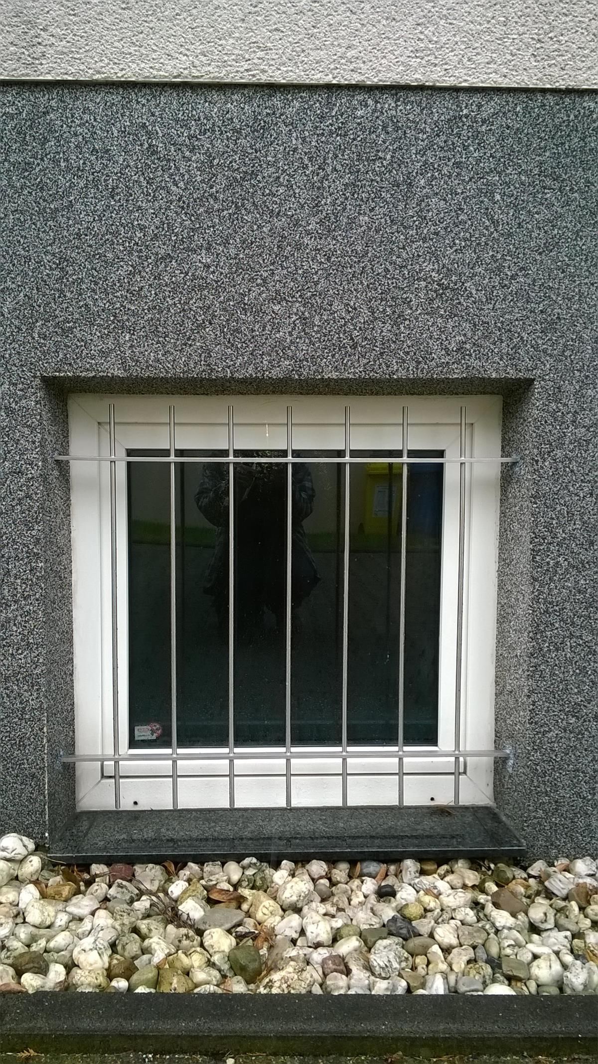 In einer grauen Wand befindet sich ein vergittertes Fenster.