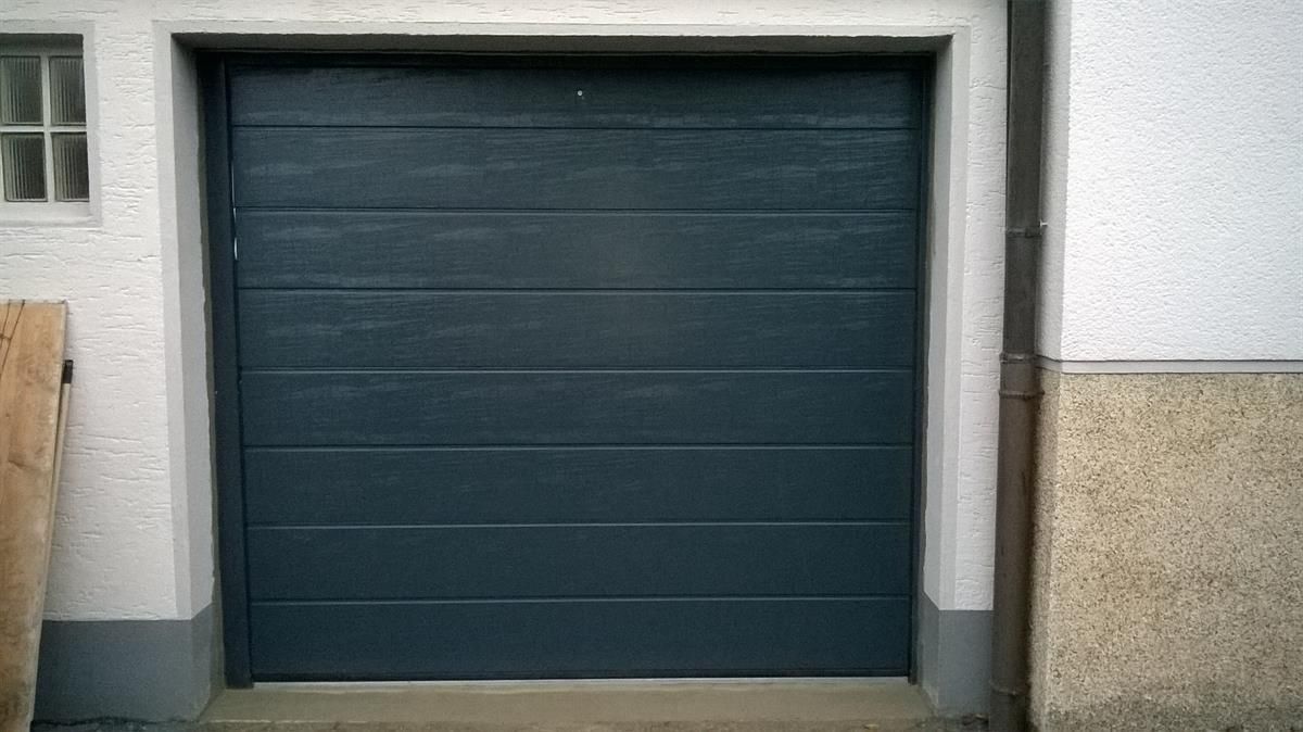 Vor einem weißen Gebäude steht ein blaues Garagentor.