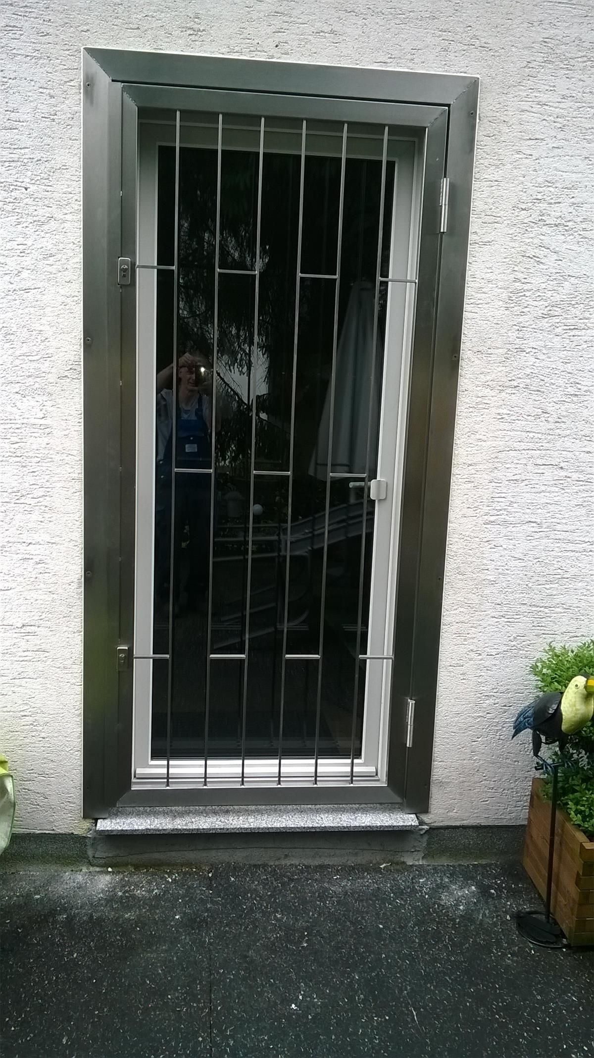 Eine Tür mit einem Metallgitter steht auf einem Gehweg neben einer Topfpflanze.