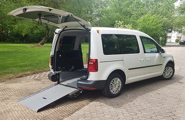 Ein weißer Lieferwagen mit einer Rampe an der Rückseite steht in einer Einfahrt.