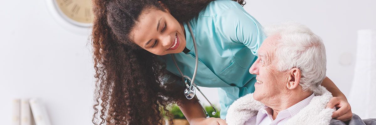 Eine Krankenschwester spricht mit einem älteren Mann im Rollstuhl.