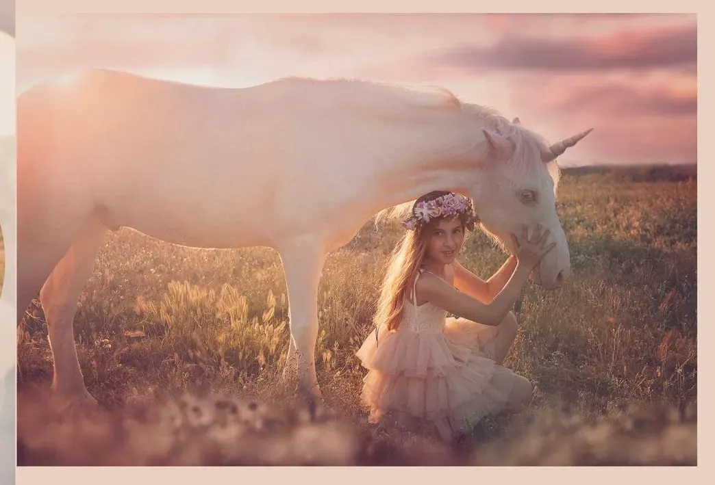 Mujer arrodillada junto a un unicornio blanco en un campo; puesta de sol en el fondo.