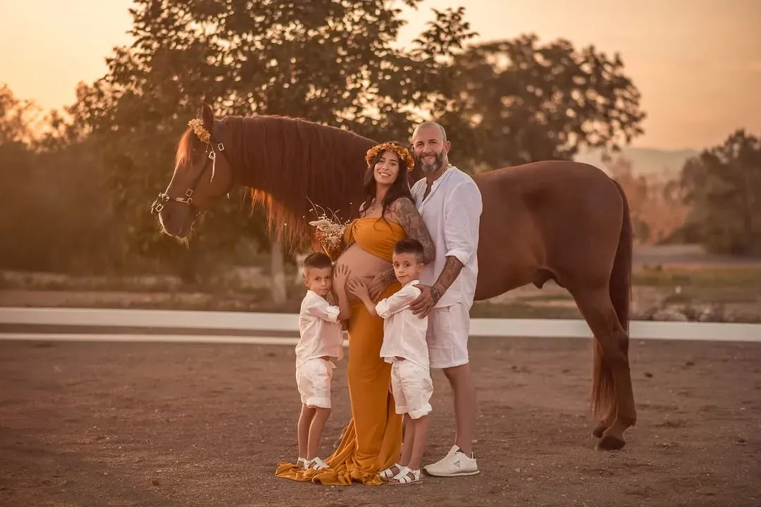 Una familia posa con un caballo en un campo dorado. Una mujer embarazada, sus hijos y un hombre sonríen.