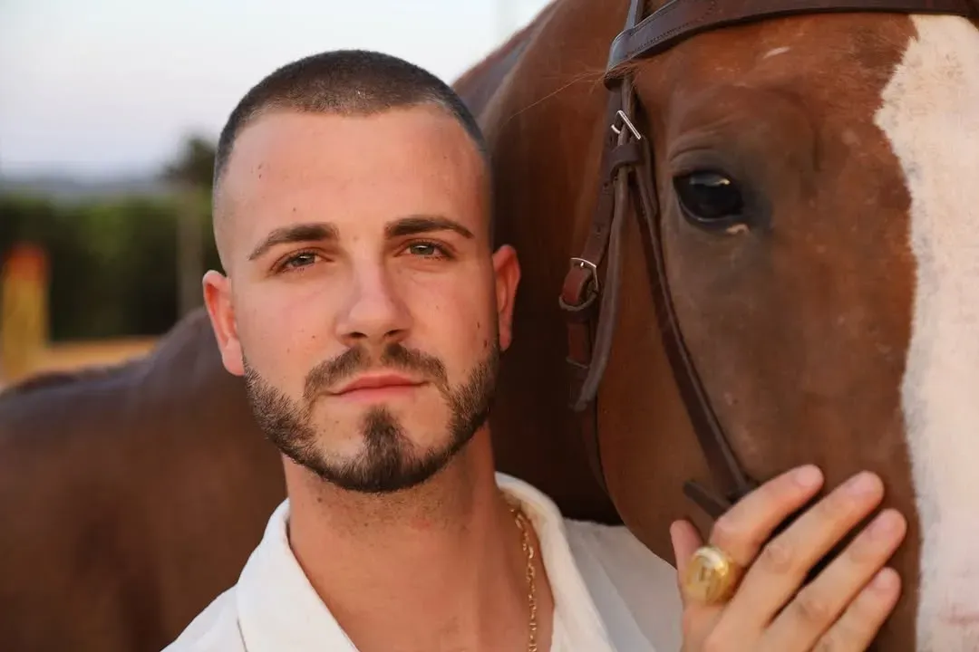 Mujer en un caballo marrón, inclinando la cabeza sobre un camino de tierra, con un sombrero negro, en el campo.