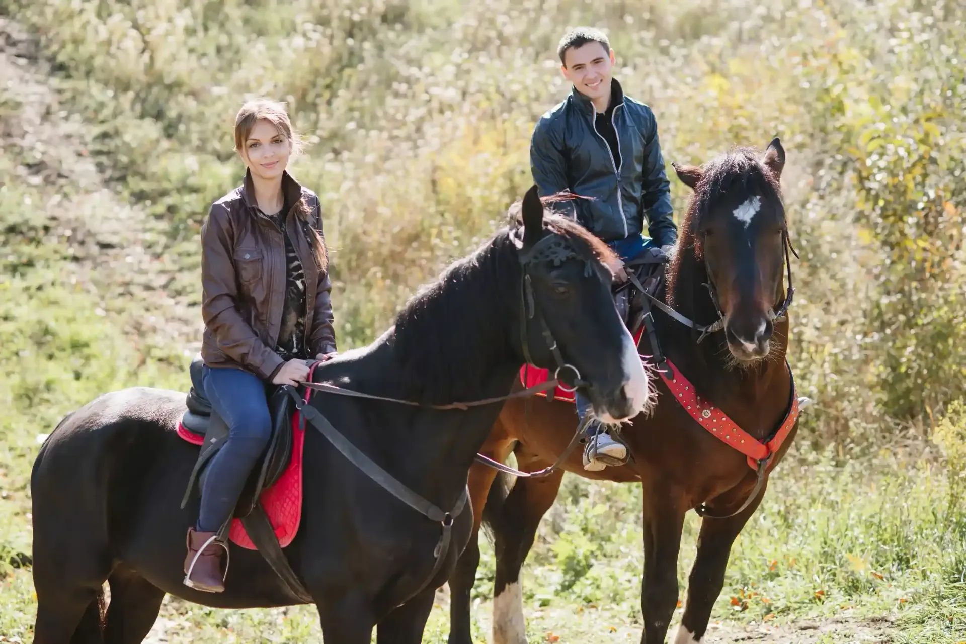 Dos personas a caballo en un entorno natural, mirando a la cámara. Un caballo es negro y el otro marrón.