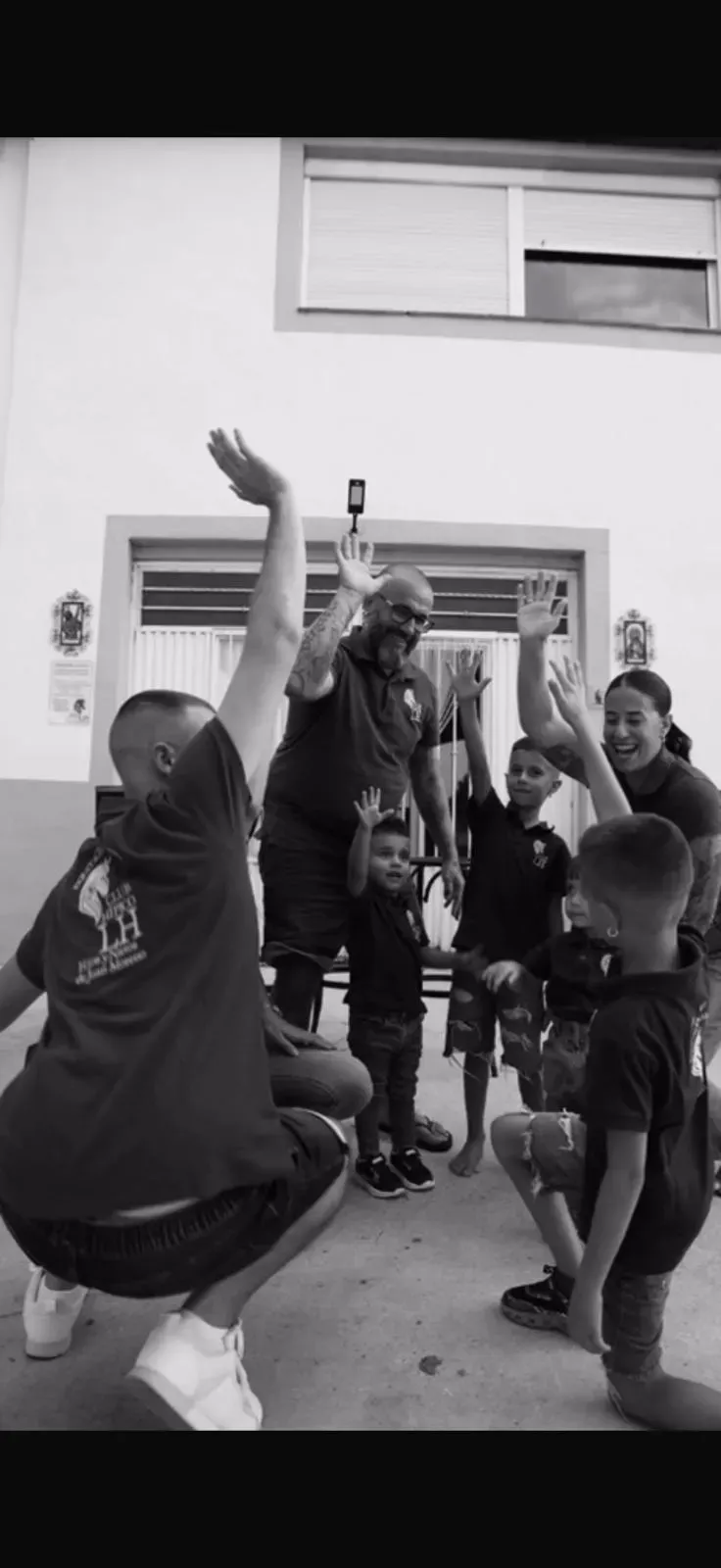 Grupo de personas con los brazos en alto posan afuera de un edificio, en blanco y negro.