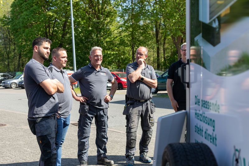 Eine Gruppe Männer steht neben einem Anhänger auf einem Parkplatz.