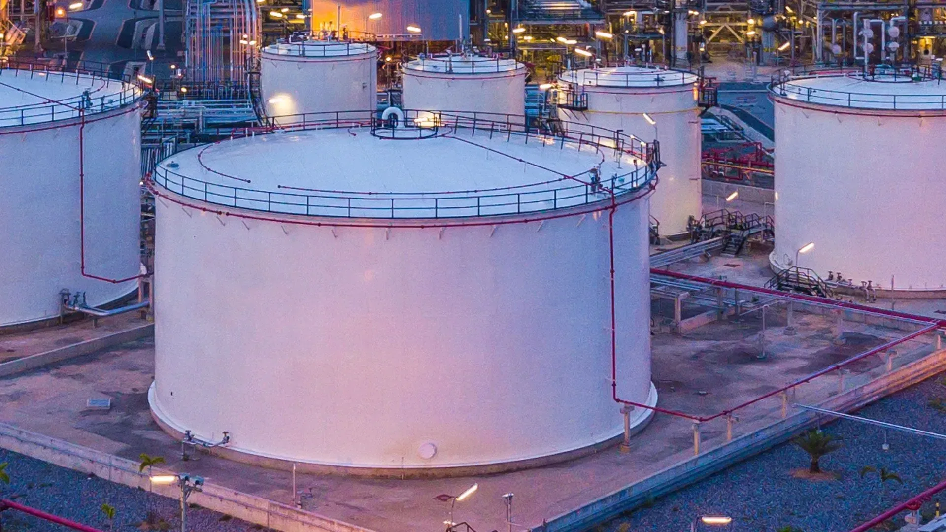 Um grupo de grandes tanques brancos estão posicionados um ao lado do outro em uma grande área industrial.