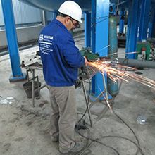 Um homem está cortando um pedaço de metal com um moedor em uma fábrica.