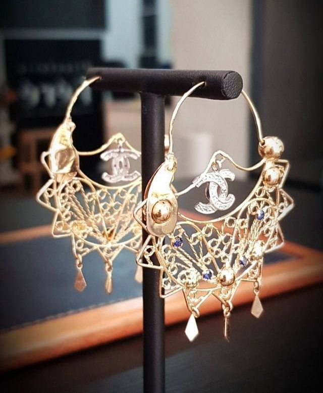 Boucles d'oreilles créoles Chanel en or, ornées de délicates broderies en filigrane, de diamants et du logo, sur un support noir.