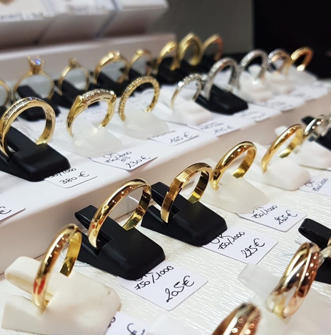 Présentoir à bijoux avec bagues en or et en argent sur des supports noirs et blancs, étiquettes de prix variées.