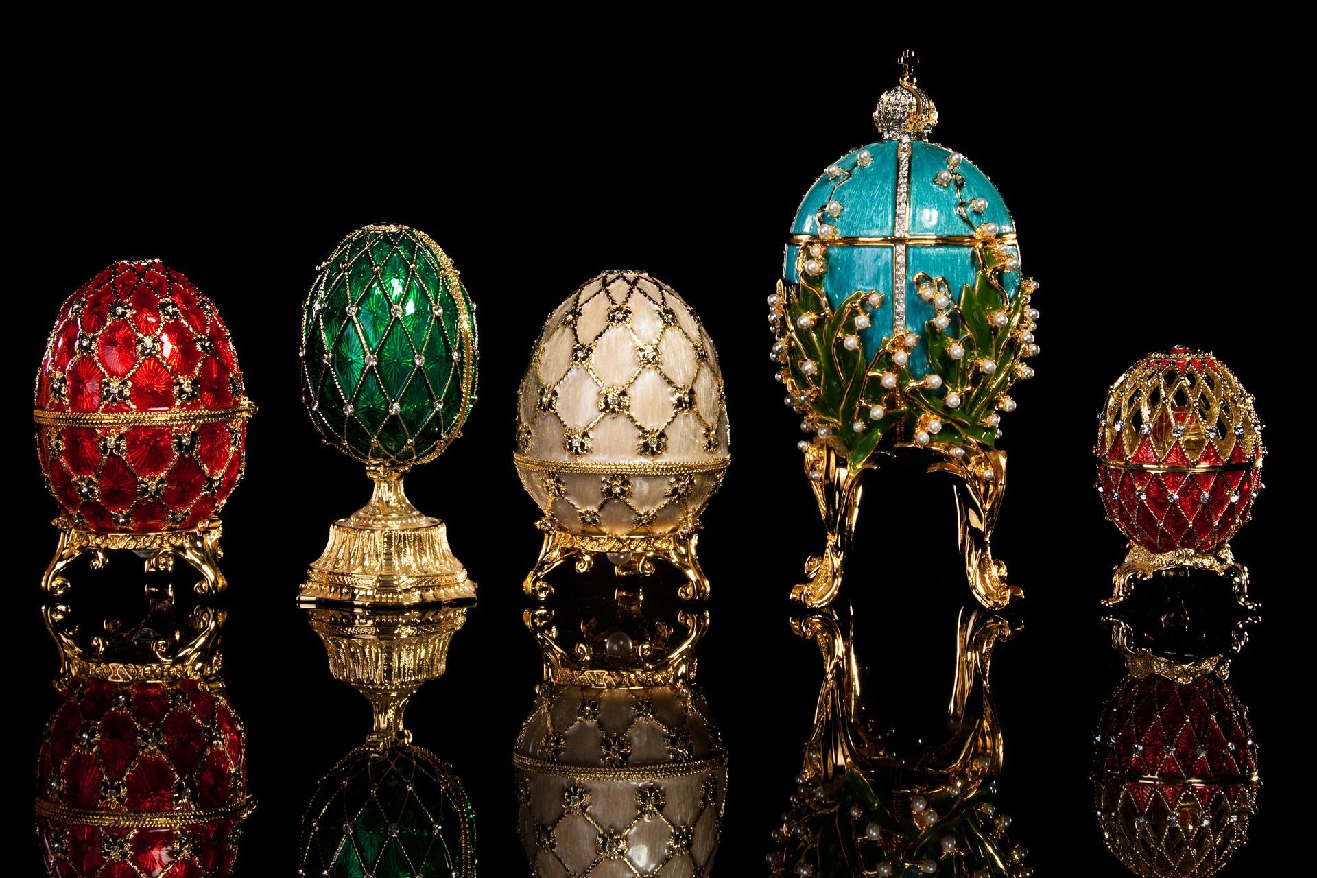 Cinq œufs Fabergé ornés de pierres précieuses sur un fond noir, chacun présentant des motifs complexes et des couleurs éclatantes.