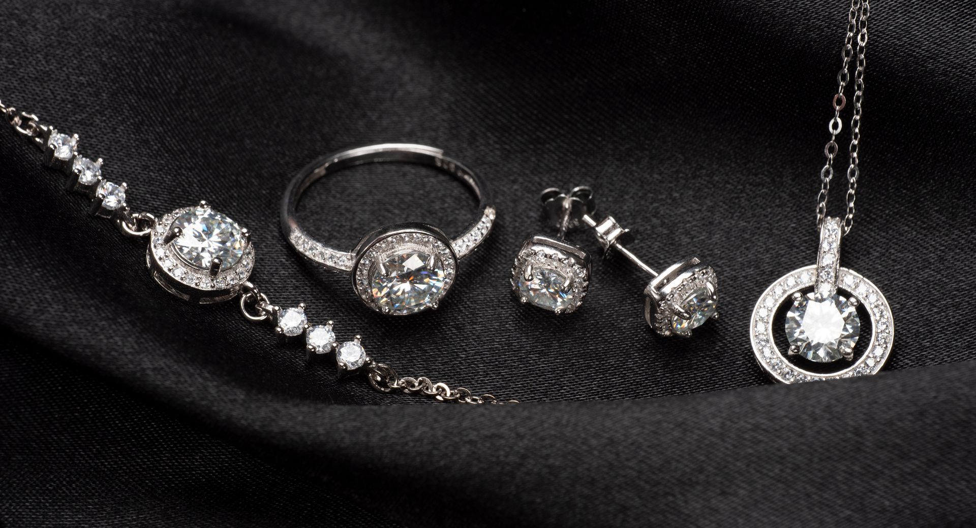 Ensemble de bijoux : bracelet, bague, boucles d'oreilles et pendentif en diamants sur un tissu noir drapé.