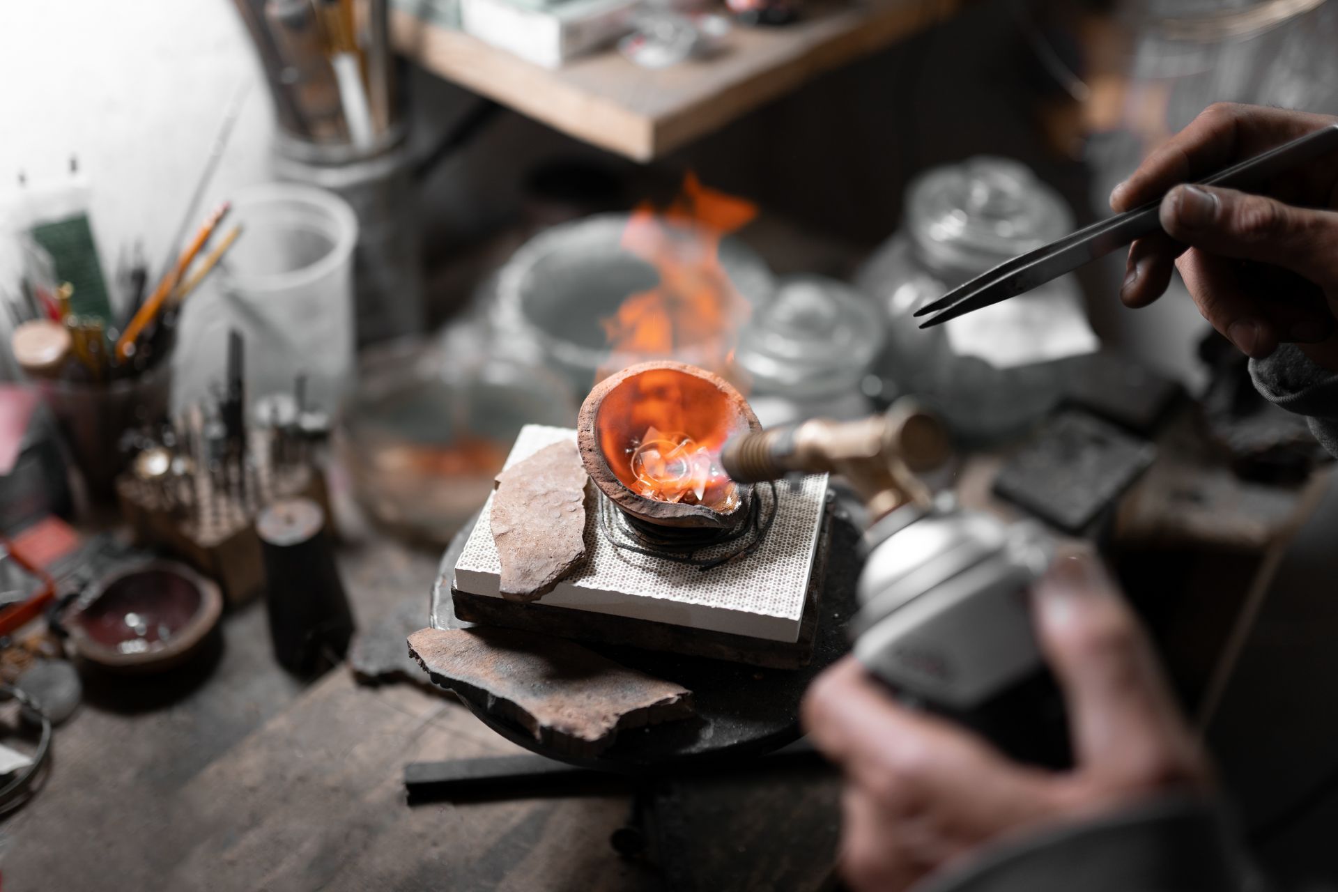 Une personne utilise un chalumeau pour chauffer un morceau de métal, fabriquant des bijoux dans un atelier.