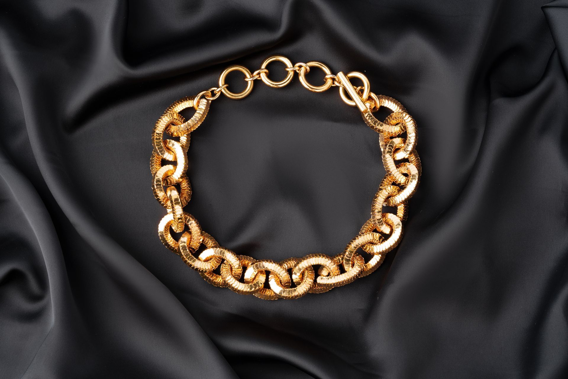 Bracelet à chaîne dorée sur tissu drapé noir.