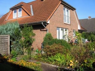 Ein Backsteinhaus mit einem roten Ziegeldach und einem Garten davor